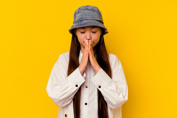 Young chinese woman isolated on yellow background praying, showing devotion, religious person looking for divine inspiration.