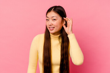 Young chinese woman isolated on pink background trying to listening a gossip.