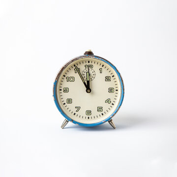 Old analog blue clock on a white background. The clock shows the time from five minutes to twelve o'clock. Copy Space. Clock. Time.