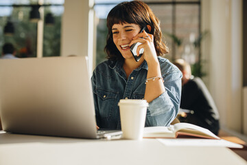 Happy businesswoman talking on mobile phone and using laptop