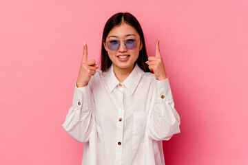 Young chinese woman isolated on pink background indicates with both fore fingers up showing a blank...