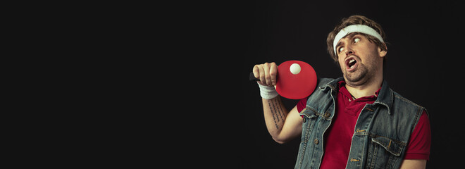 Young Caucasian funny man playing ping pong isolated on black background. - obrazy, fototapety, plakaty