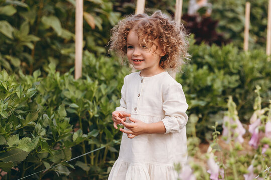 beautiful little girl with curly hair posing for photo walking among the flowers in nature