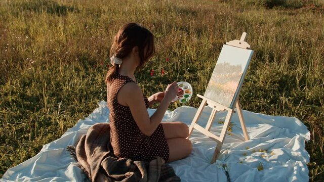 Ragazza dipinge un panorama su tela seduta nel prato