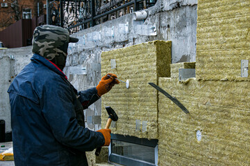 A man installs a layer of thermal insulation on the wall of the stairs outside - using mineral wool...