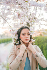 Portrait of a beautiful young woman in blooming sakura at sunset. Spring.