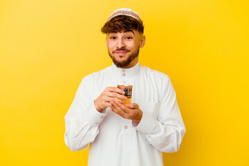 Young Moroccan man wearing the typical arabic costume drinking tea isolated on yellow background
