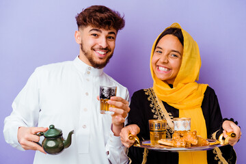 Young Moroccan couple drinking tea celebrating ramadan month isolated on purple background