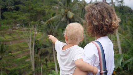 Back view of a Caucasian woman holding her baby looking at the jungle landscape.Blonde baby pointing far away 