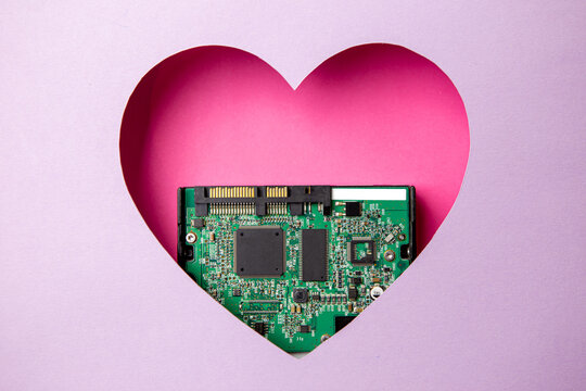 The green printed circuit board with microprocessors is located in a pink heart-shaped cavity. All around is purple. Copy Space. Love. Technology. Artificial intelligence. Robotics.