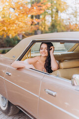 Portrait of a brunette bride sitting in a pink car in the back seat and smiling. Concept of bride