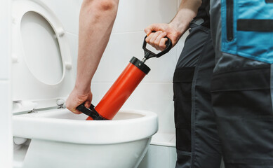 Plumber unclogging toilet with professional force pump cleaner.
