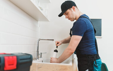 Plumber unclogging kitchen sink with professional force pump cleaner.