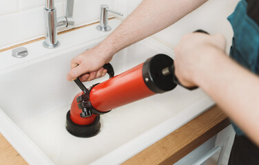 Plumber unclogging kitchen sink with professional force pump cleaner.