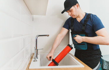 Plumber unclogging kitchen sink with professional force pump cleaner.