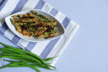 a plate of fried crispy green beans served with chili flakes in white background