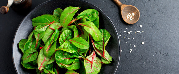 Fresh swiss chard leaves or mangold in black ceramic dish on dark concrete background. Concept for...