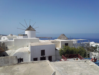 Fototapeta na wymiar Typical view of town located in Oia during day with terrace roof in front against wind mill on Santorini, one of the Cyclades islands in Aegean Sea, Greece