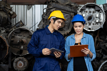Fototapeta premium Group of young Asian male and female employee worker using clipboard checking old automotive spare parts, engine, motor, machine at the garage industry factory or automotive spare parts warehouse