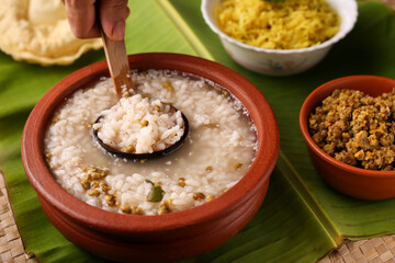 Rice porridge, Kanji, gruel in clay pot palm mat background Kerala South India.  congee, rice soup, green gram curry, chammanthi.  Hand serving Ayurveda diet for immunity.  Indian Sri lankan veg food.
