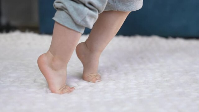 feet baby learns to walk. indoor first steps of a newborn close-up at home. baby feet kicking learns to walk. A cute boy learns to walk and take his first steps. concept newborn close-up