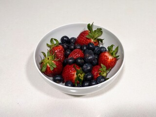 White bowl of strawberries and blueberries on a white colored table