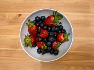 White bowl of strawberries and blueberries on a wooden table.