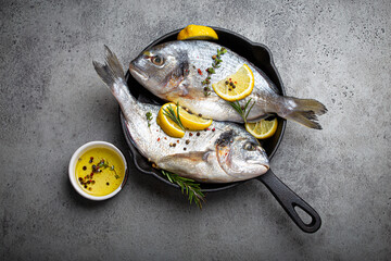 Raw fresh fish sea bream or dorado with lemon, thyme, rosemary and seasonings in cast iron skillet...