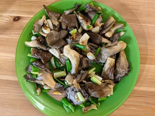 Sautéed mushrooms with organic green garlic and healthy food in a ready-to-eat dish on a wooden table.  Pleurotus eryngii
