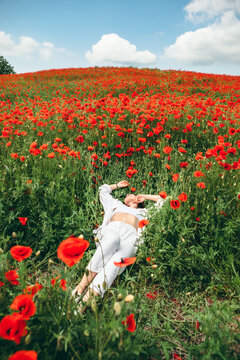 young pretty woman laying down at the field of poppy flowers