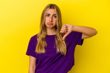 Young blonde caucasian woman isolated on yellow background showing a dislike gesture, thumbs down. Disagreement concept.
