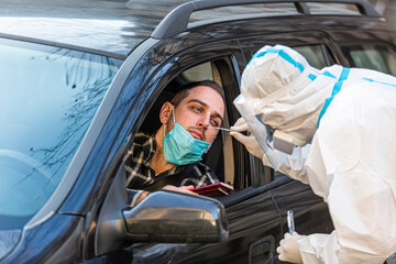 Man showing passports, medical worker in PPE performing drive-thru COVID-19 test