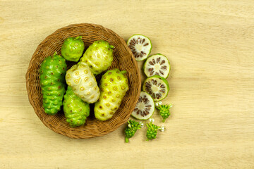 Pile of Noni fruit or Morinda Citrifolia on Wicker basket on wooden background, Top view. Fresh noni are high nutrients and antioxidants.