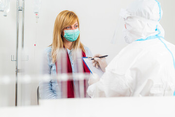 Medical worker in PPE examining patient for COVID-19 in hospital lab.