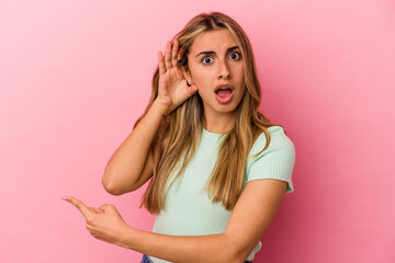 Fototapeta premium Young blonde caucasian woman isolated on pink background trying to listening a gossip.