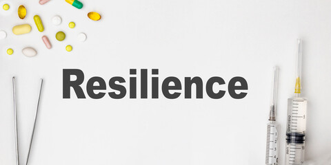 RESILIENCE - text written on a white background. pills, tweezers, a syringe lie next to the table. Medical and health care concept.