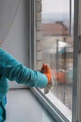 A woman in an orange glove wipes the window with a rag. The concept of cleanliness in the house