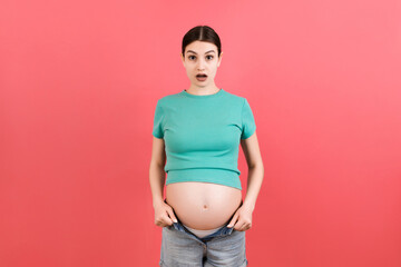 pregnant woman in unzipped jeans showing her naked abdomen at colorful background with copy space