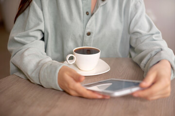 Tablet close up photo with woman hands. Girl using tablet at home or in cafe and drinking coffee
