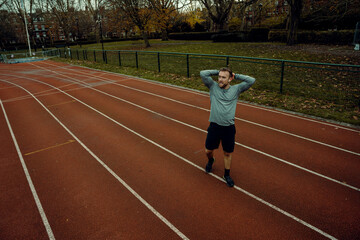 Obraz premium Caucasian male athlete holding hands behind head walking on tracking field