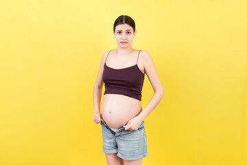 pregnant woman in unzipped jeans showing her naked belly at colorful background with copy space. Baby expecting concept