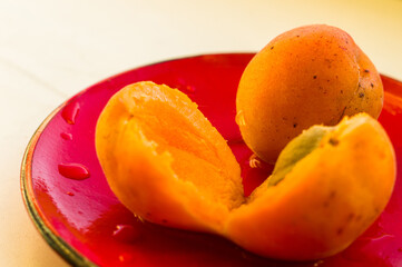 halves of a large fresh apricot on a red saucer, close-up