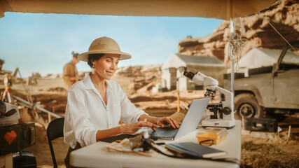 Fototapeta na wymiar Archaeological Digging Site: Beautiful Female Archaeologist Doing Research, Using Laptop, Analysing Fossil Remains with Microscope. Historians Excavating Site of Great Diverse Ancient Civilization
