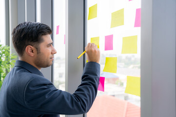 Business man is working and brainstroming in the meeting room with colleauge. Using agile methodology and do business model canvas . Colorful sticky notes on the wall are posted for new idea