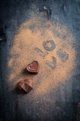 heart-shaped chocolate candy, viewed from above and side with cocoa on wooden base