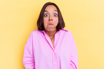 Young mixed race woman isolated on yellow background shrugs shoulders and open eyes confused.