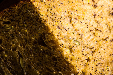 Slice of rustic natural yeast-free bread with flax, poppy seeds, sesame seeds, millet, pumpkin and sunflower seeds, on a black background, hard light, photo in a low key, close up.