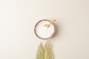 Collagen powder in bowl with measure spoon with palm leaves on pastel beige background. Flat lay, copy space