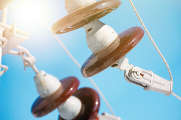 A ceramic suspended insulator hangs from a power line against a blue sky.