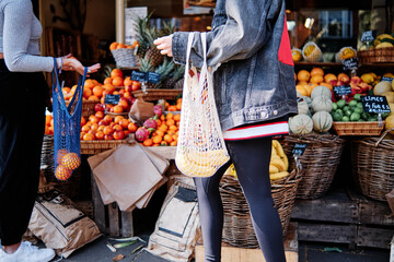 Women with eco friendly bags buying fruits on street market